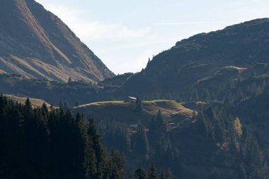 Etrafı dağlarla çevrili küçük yeşil bir tepenin tepesindeki kırsal bir evin insansız hava aracı görüntüsü.