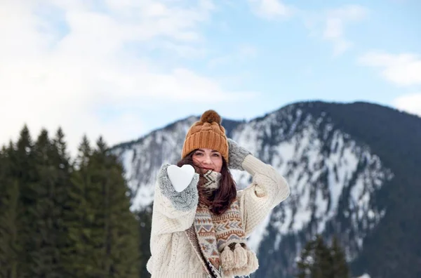 スカーフと冬の帽子をかぶった女性の観光客は カメラに向かってハート型の雪玉を保持します — ストック写真
