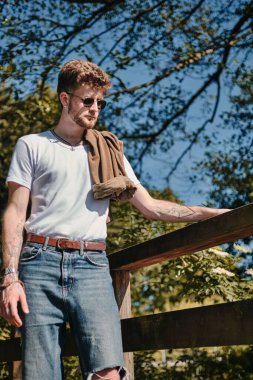 Kafkasyalı bir adamın arka planda ağaçlar olan ahşap bir çitin yakınındaki dikey görüntüsü.