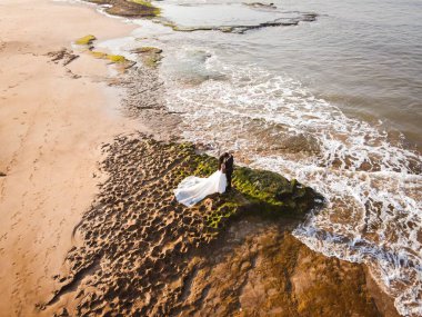 Gelin ve damadın güzel kumlu bir sahil kıyısında birlikte yürüdükleri hava manzarası.