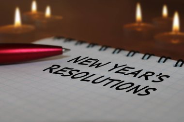 Yanan mumlara karşı ahşap masa üzerinde bir defter ve kalem. Yeni yıl için çözümler.