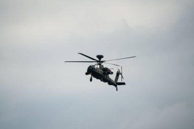 Koyu gri bir ordu saldırı helikopteri gündüz uçuyor.