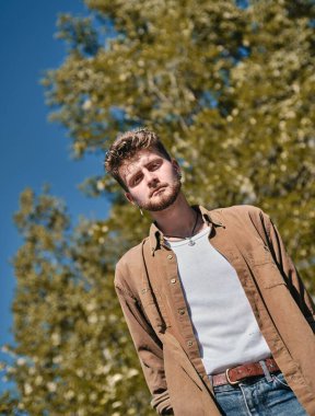 Beyaz bir adamın arka planda bulanık bir şekilde kameraya baktığı dikey alçak açılı bir çekim.