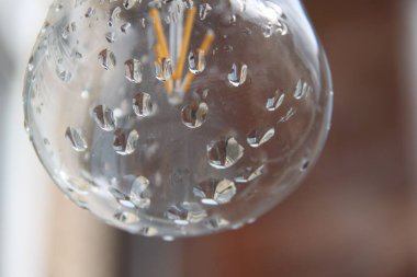 Bir ampulün üzerindeki saydam yağmur damlalarının yakın çekimi