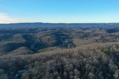 Etrafı verimli ormanlarla çevrili asfalt bir yolun insansız hava aracı görüntüsü.