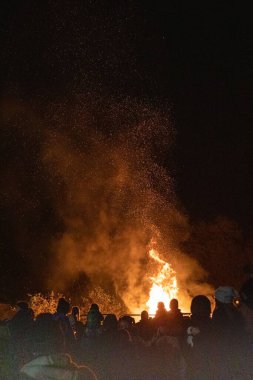 Kalabalığın dikey görüntüsü gecenin kükreyen ateşinin önünde duruyor.