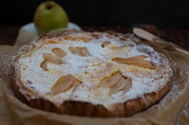 Yakın plan vanilyalı armutlu turta. Arka planda bir armut var.