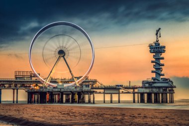 De Pier, Scheveningen İskelesi açık hava güverteleriyle kumsalda bulutlu gün batımına karşı