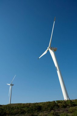 Mavi gökyüzü arka planına sahip bir tepedeki Rüzgar Gücü Türbininin dikey görüntüsü