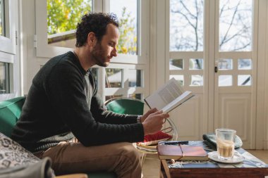 Kafkasyalı adamın kanepede oturup kitap okuduğu dikey bir fotoğraf.