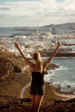 Mavi deniz manzaralı, Gran Canaria adasına karşı poz veren mutlu bir kızın dikey görüntüsü.