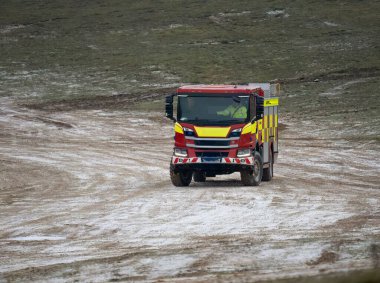 Kırmızı ve sarı bir itfaiye aracı off-road yolunda sürülüyor.