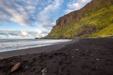 Deniz dalgaları Vik, İzlanda 'da bulutlu bir gökyüzünün altında kara kumlara yaklaşıyor.