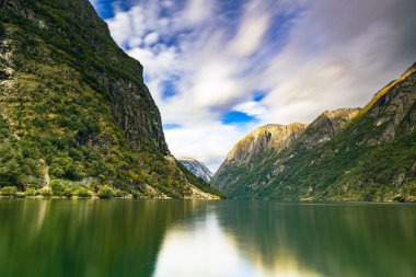 Gökyüzü arka planında gölle çevrili devasa kayalık dağların manzarası.