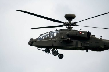 Koyu gri bir ordu saldırı helikopteri gündüz uçuyor.