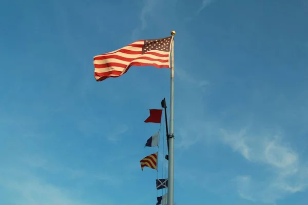 Mavi Gökyüzünün Altında Diğer Bayraklarla Birlikte Yüksek Metalik Bir Direkte — Stok fotoğraf
