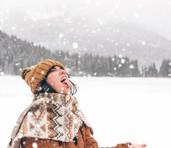在寒冷的荒野里 一个戴着温暖的冬帽和围巾的女人在雪地里伸出舌头 — 图库照片