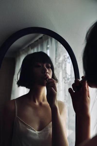在一间灯光暗淡的房间里 一个性感迷人的中国女人把口红贴在镜子上的画像 — 图库照片