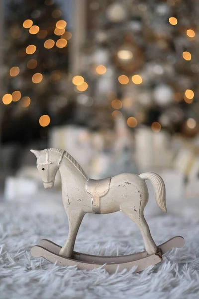 A closeup shot of a small rocking horse figure on a fluffy carpet, with bokeh lights in the background
