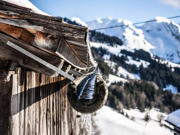 一张特写照片 拍的是锈迹斑斑的木制排水沟和屋顶 后面是雪山覆盖 — 图库照片