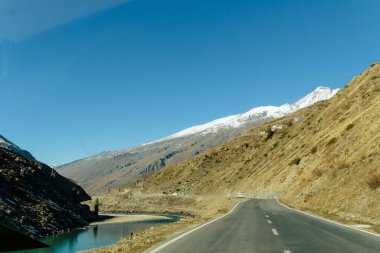Dağlarda kar ve ağaçlar mavi gökyüzü ve bulutlar bir arka plan üzerinde yolun kenarında kaplı asfalt yoldan doğal kış görünümü