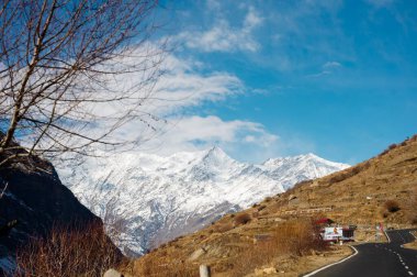 Dağlarda kar ve ağaçlar mavi gökyüzü ve bulutlar bir arka plan üzerinde yolun kenarında kaplı asfalt yoldan doğal kış görünümü