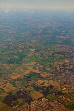 Bir uçaktan gündüz vakti yeşil alanların, binaların ve yolların dikey görüntüsü.