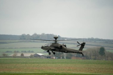 Koyu gri bir ordu saldırı helikopteri gündüz uçuyor.