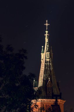 Uzun bir kilise kulesinin dış cephesi. Geceleri ağaçlarla kesişen, dikey çekim.