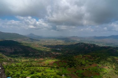 Bulutların gölgesi altında ekili tarım arazileri ve evleri olan bir kırsal alanın hava görüntüsü.