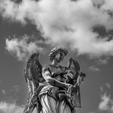 Gri tonlu bir melek heykeli gündüz gökyüzüne ve bulutlara karşı