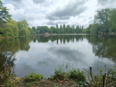 Büyük yeşil ağaçlarla çevrili küçük gölü olan güzel bir park.