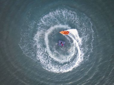Bir deniz yüzeyinin havadan görünüşü. Yüzen bir yatakta yatan bir çift ve onları çevreleyen bir tekne.