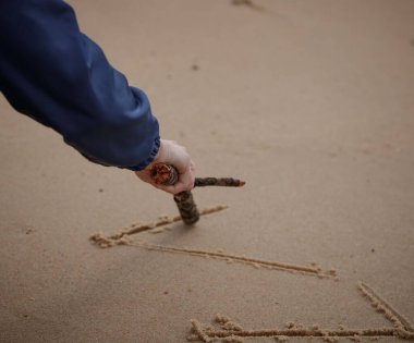A high angle shot of a human's hand writing something with the help of a branch clipart