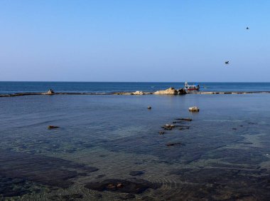 Güneşli bir günde sahilde yelken açan bir teknenin manzarası.