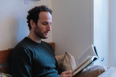 Kafkasyalı adam kanepede oturup kitap okuyor.