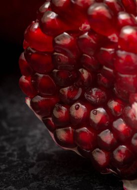 Dikey bir makro çekim. Nar kabuğuna istiflenmiş sulu bir tohum. Siyah bir zemin üzerinde.