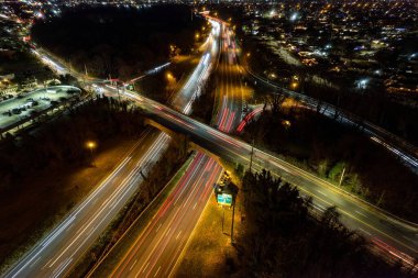 Gece aydınlık yolların hava görüntüsü, arabaların ışıklarının uzun pozlu görüntüsü, arka planda gece manzarası.