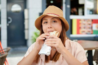 Açık hava restoranında burrito yiyen İspanyol bir kadın.