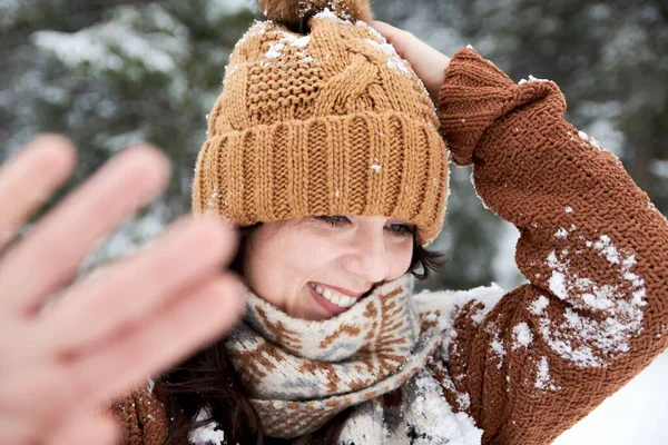 一个穿着舒适的冬季毛衣和帽子的女人笑着对着摄像机挥手 毛衣上还挂着雪 — 图库照片