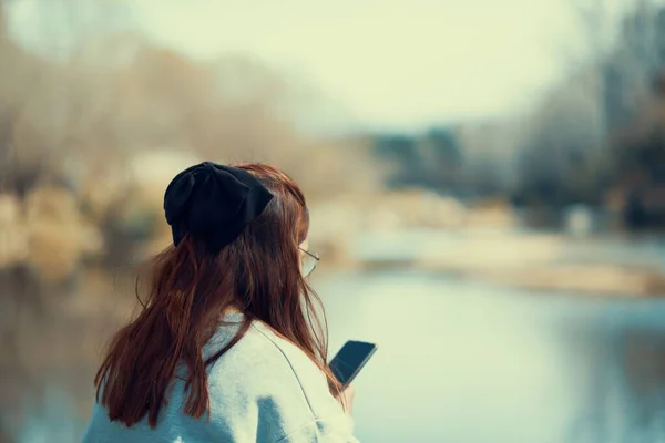 Naturskøn Udsigt Kvinde Kigger Ned Hendes Telefon Ved Siden Flod - Stock-foto