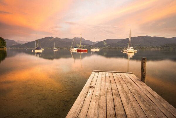 A jetty with sailing boats in the water at sunset.