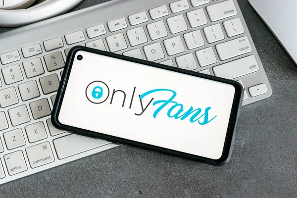 Üzerinde Onlyfan logosu olan düz bir akıllı telefon yatağı beyaz bir klavye ve gri bir masa