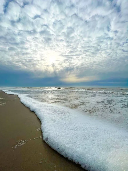 Вертикальный Снимок Пенного Пляжа Солнечными Лучами Видимыми Сквозь Облака — стоковое фото