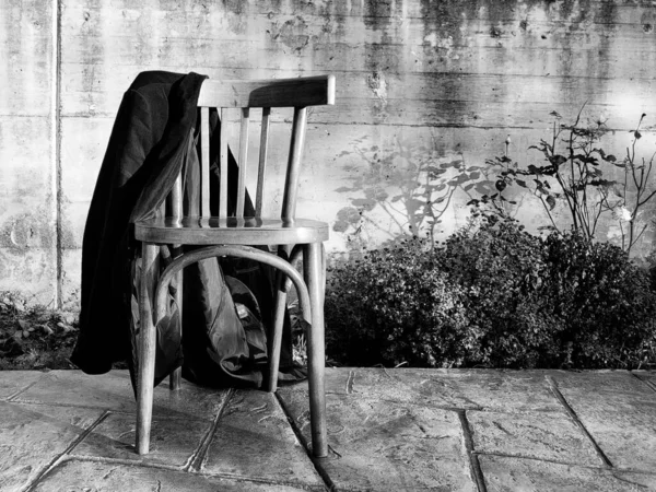 一张深色的旧木椅的照片 在房子的院子里 上面有一件黑色的夹克 — 图库照片