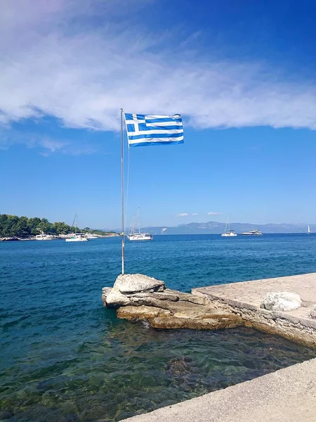 Pionowe Ujęcie Skalistego Molo Grecką Flagą Trzepoczącą Biegunie Tle Zacumowanych — Zdjęcie stockowe