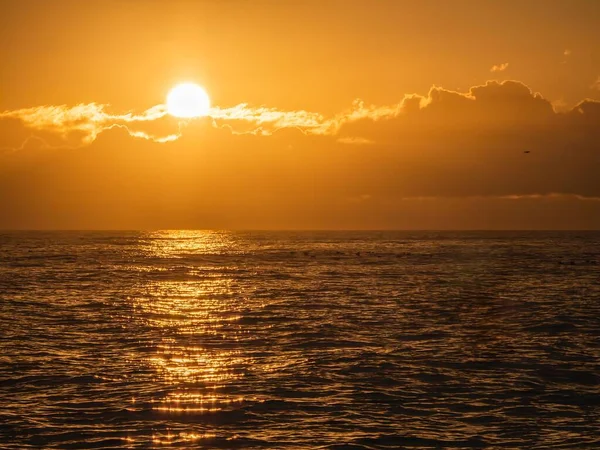 背景には曇り空のオレンジ色の空が広がる海岸沿いの美しい夕日 — ストック写真