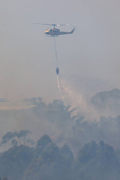 A vertical shot of a huey helicopter dropping a water bag on flames