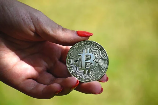 背景のぼやけた背景に銀ビットコインを保持する女性の手 暗号通貨の概念 — ストック写真