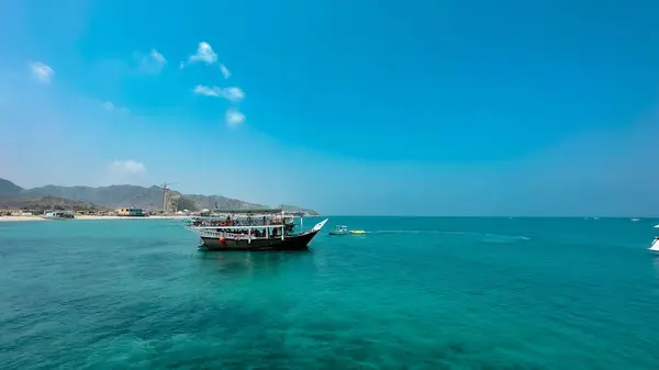 stock image A big boat swimming in the waters of the blue sea in Fujairah with mountains in the background